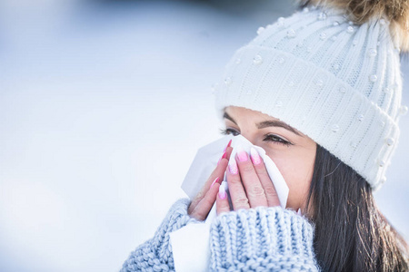 有吸引力的年轻女人在冬天用纸巾吹鼻子。