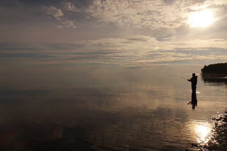 日落时渔夫的剪影。在湖上钓鱼