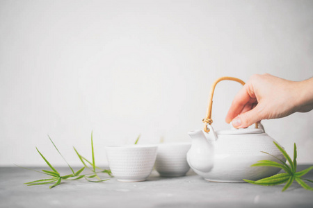 女性手把绿茶从茶壶倒入白色背景上的杯子，并有复制空间。 亚洲茶具。