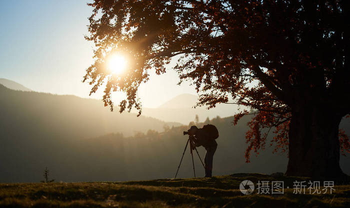 和专业照相机拍摄旅游摄影师的剪影,并在日落背景上拍摄山脉全景图