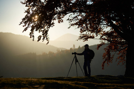 专业照相机拍摄旅游摄影师的剪影,并在日落背景上拍摄山脉全景图照片
