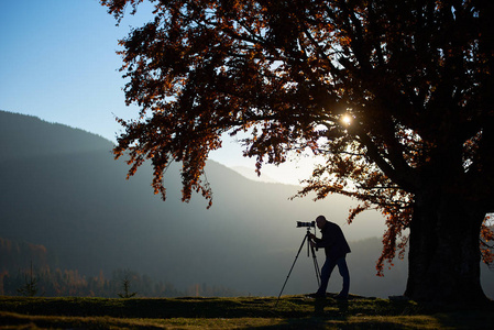 旅游摄影师用三脚架和专业相机剪影,在日落背景下拍摄山脉全景照片