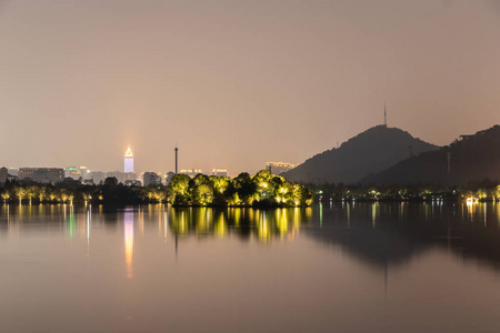 湖和城市的夜景。 湖面上有光的树，高高的发光的摩天大楼，群山。 湖中的倒影。 美丽的夜景。