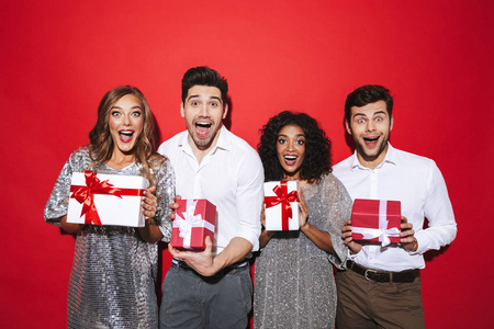 四个穿着得体的快乐朋友站在红色背景下庆祝礼物箱