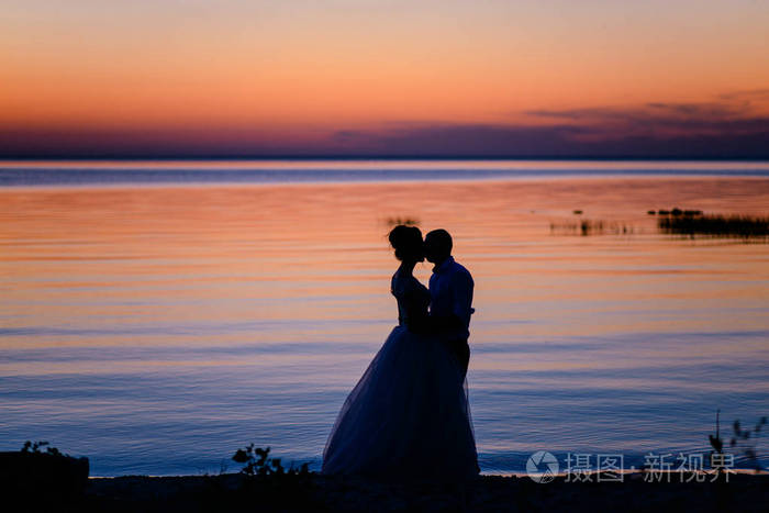 在日落时分,两个情人在水的背景下拥抱