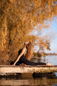 年轻女子在秋天公园的安静码头练习瑜伽。