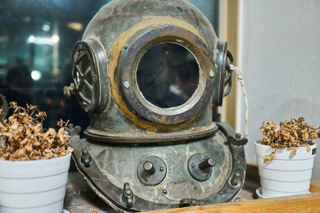 老式潜水头盔，生锈的金属展示在架子上，两边都是干花。