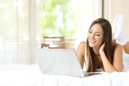 幸福的女人躺在床上，在家里或公寓里用笔记本电脑
