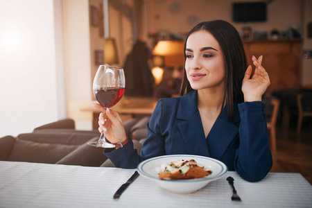 美丽的年轻女商人坐在餐厅的桌子旁。她向左看。顾客手里拿着一杯红酒。桌上的沙拉碗