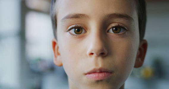 特写一个小男孩的肖像,棕色的眼睛看着厨房背景上的相机.