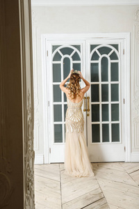 美丽的黑发模特身着米色连衣裙，站在豪华内部靠近白色门的地方