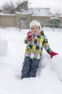 男孩在雪地里玩。 婴儿在冬天玩雪。 穿着蓝色夹克和五颜六色帽子的小学步男孩在圣诞节的冬季公园里捉雪花