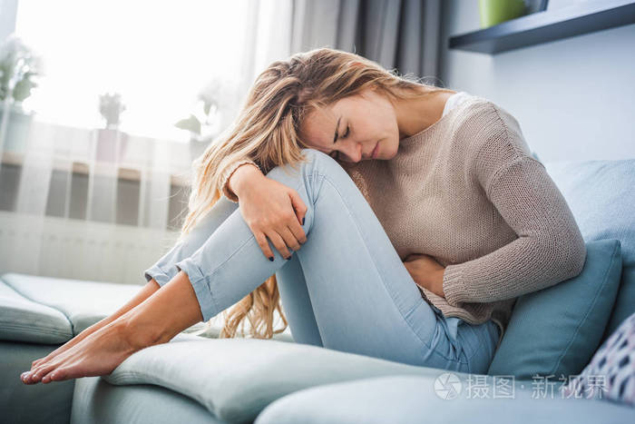 在家坐在沙发上的年轻女子,腹部剧烈疼痛