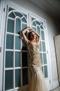 美丽的黑发模特身着米色连衣裙，站在豪华内部靠近白色门的地方