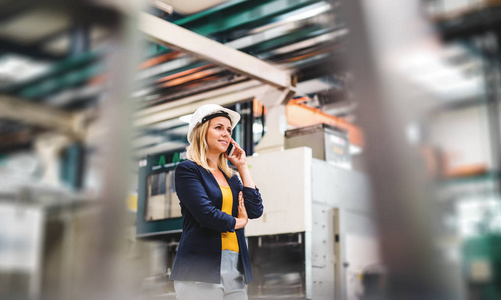 一位工业女工程师在电话中的画像, 站在工厂里