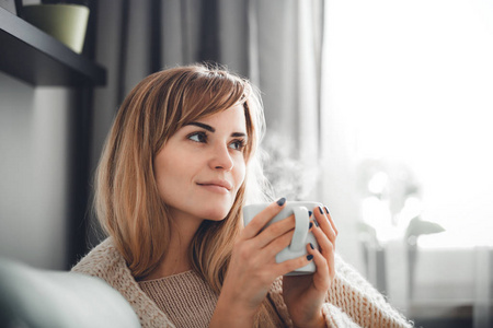 快乐的女人穿着柔软的毛衣，带着一杯热茶或咖啡在