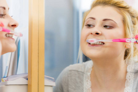 女人刷牙刷牙特写。 带牙刷的金发女孩在浴室里看镜子。 口腔卫生。