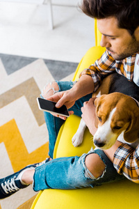 帅哥在沙发上和狗坐在一起时用智能手机