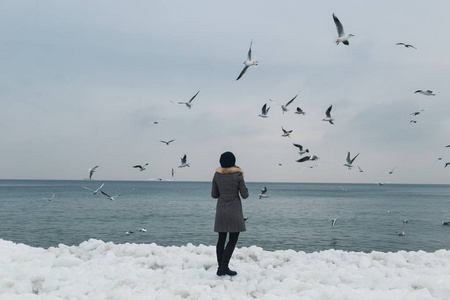 一个女孩在冬天结冰的海边喂海鸥。人与鸟的概念。