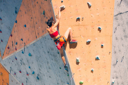 在城市攀岩健身房训练。 一个强壮的女人在人工地形上爬上一条攀岩路线。 苗条的女孩参与运动。