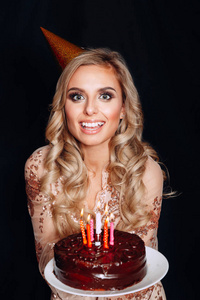 一个年轻美丽的金发女孩拿着生日蛋糕与蜡烛在黑色背景的肖像