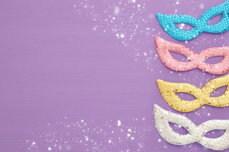 嘉年华派对庆祝概念与彩色粉彩，粉红色，金银和蓝色面具，紫色的木制背景。 顶部视图