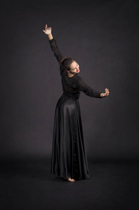 一个穿着黑色西装跳舞的年轻女孩，现代舞蹈。工作室拍摄于黑暗背景上的孤立图像。