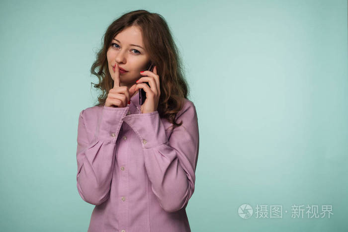 年轻有魅力的女人拿着手机，在背景图像上显示沉默的手势