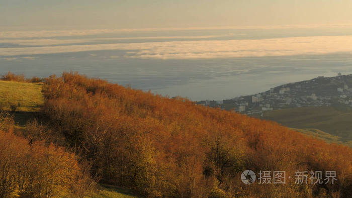 全景的风景秀丽的秋天谷从一个陡峭的浓密的斜坡上的日落天空背景。拍摄。壮观的山景的一个小村庄和田野在日落金色的光