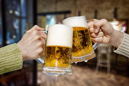 两只手正在玻璃杯与新鲜泡沫啤酒在舒适的PAB内部背景。概念是休闲时间..