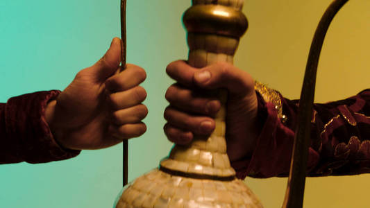 人的手给东方陶瓷水罐在蓝色和黄色的背景, 古董商品销售的概念。股票。经过东方古代陶瓷茶或酒罐的工艺