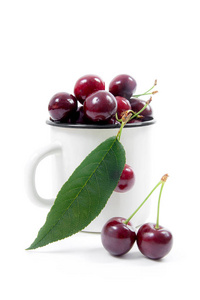 白色的杯子里有成熟的红甜樱桃浆果和几个浆果在杯子前面。白色背景下的构图