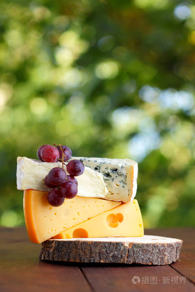 卡蒙伯特布里硬奶酪和蓝色奶酪在木板上各种奶酪和葡萄片在模糊的背景