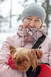 快乐的女人抱着约克郡猎犬在冬季公园户外，专注于女人