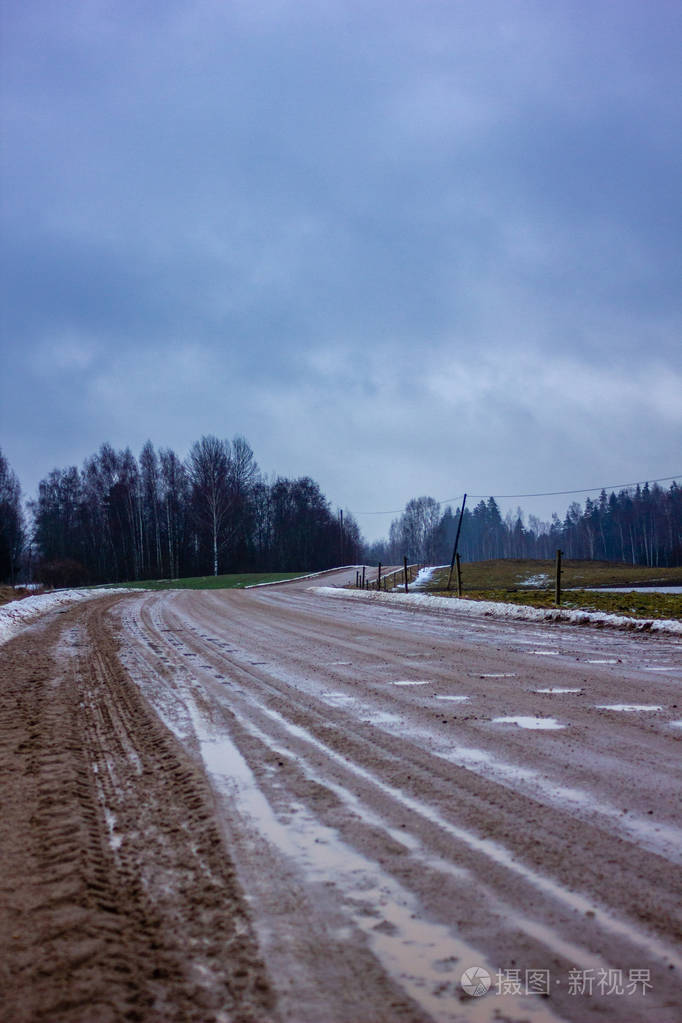 在阴天的冬日里空旷的乡村景观雪部分覆盖着地面雾坑和路上的轮胎痕迹