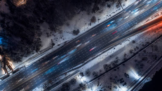 从上到下的夜行路, 在冬季公园之间有大灯的路过的汽车