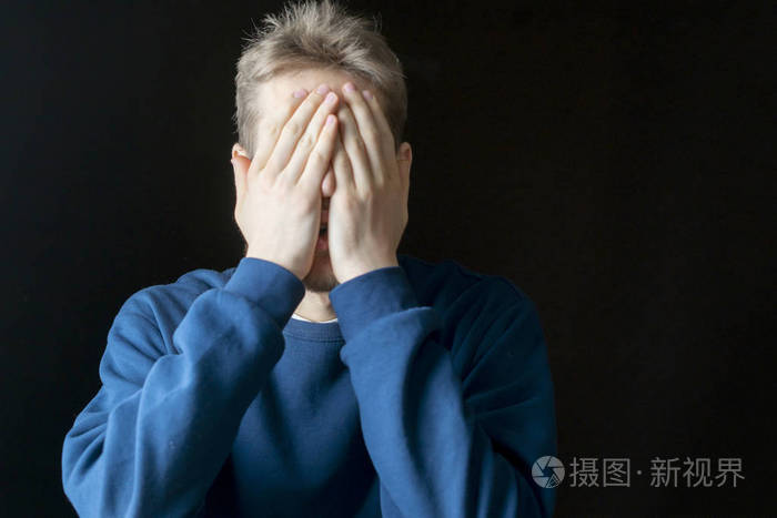 年轻而悲伤的男性用双手捂住他的脸在黑暗的背景上
