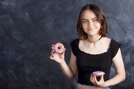 黑色背景上有甜甜圈的快乐女孩的肖像。快乐的女孩拿着新鲜的甜甜圈微笑着。好心情，饮食观念..
