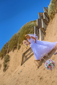 新娘穿着白色婚纱，捧着花束，在美丽的海滩上摆姿势。