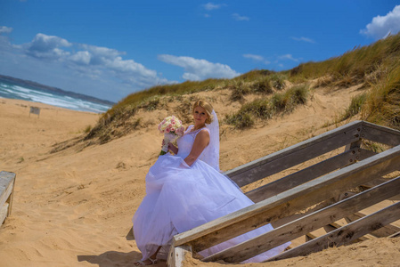 新娘穿着白色婚纱，拿着花束，在美丽的海滩上摆姿势。