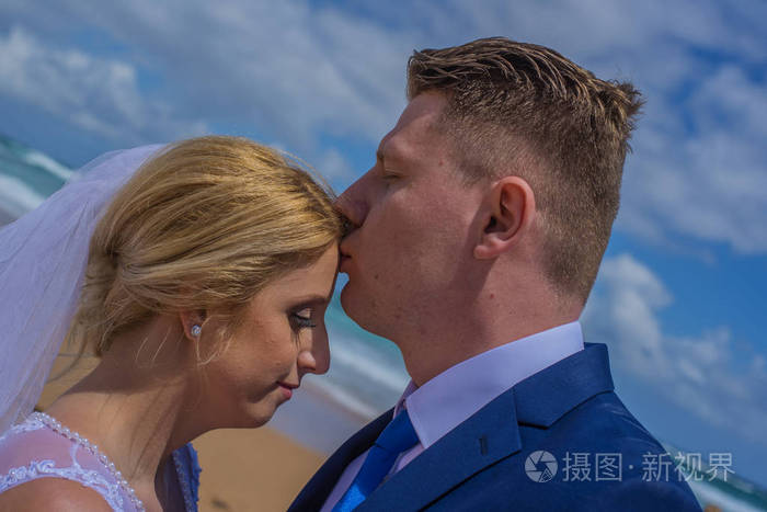 刚结婚的男人在额头亲吻他的妻子射向澳大利亚沙滩
