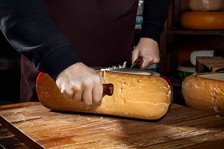 一个年轻的工人在商店里切了一半的奶酪。木质背景，奶酪刀。特写镜头。复制文本徽标或品牌的空间。工作理念。