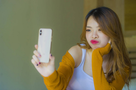 年轻有魅力放松的亚洲女孩在家卧室里享受自拍肖像照片，手机相机坐在床上做着青少年学生生活方式的面孔