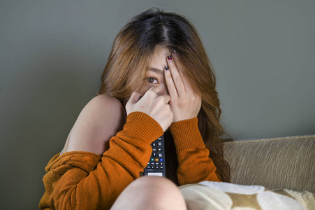 年轻迷人可爱害怕的亚洲女人独自在家客厅沙发上看恐怖电影或电视剧