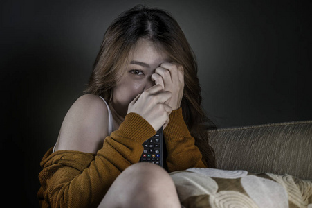 年轻,迷人,可爱,害怕的亚洲女人独自在家客厅沙发上看恐怖电影或电视