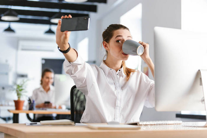 快乐的年轻女商人坐在办公室的工作场所自拍喝咖啡