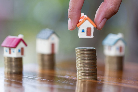 人手把房子模型放在硬币堆叠上，计划储蓄硬币，购买房屋概念抵押贷款和房地产投资。 为房子储蓄或投资。