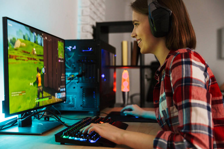 兴奋的女孩游戏玩家坐在桌子旁,在室内电脑上玩网络游戏照片