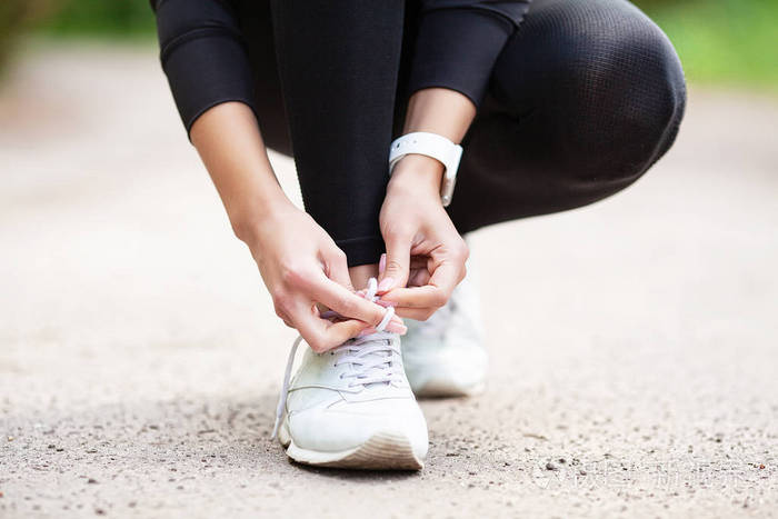 健身.女子跑者紧固鞋线.跑步者女子脚在路上跑步特写镜头上的鞋子