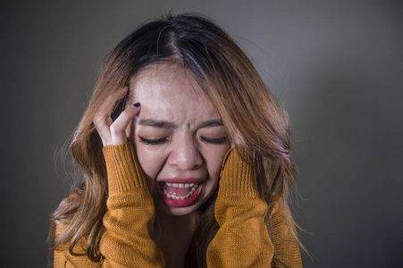 年轻的疯狂绝望和沮丧的亚洲韩国妇女尖叫，恐惧和焦虑，愤怒和痛苦孤立在黑暗的背景上，剧烈的疼痛，面部表情，抑郁的概念。